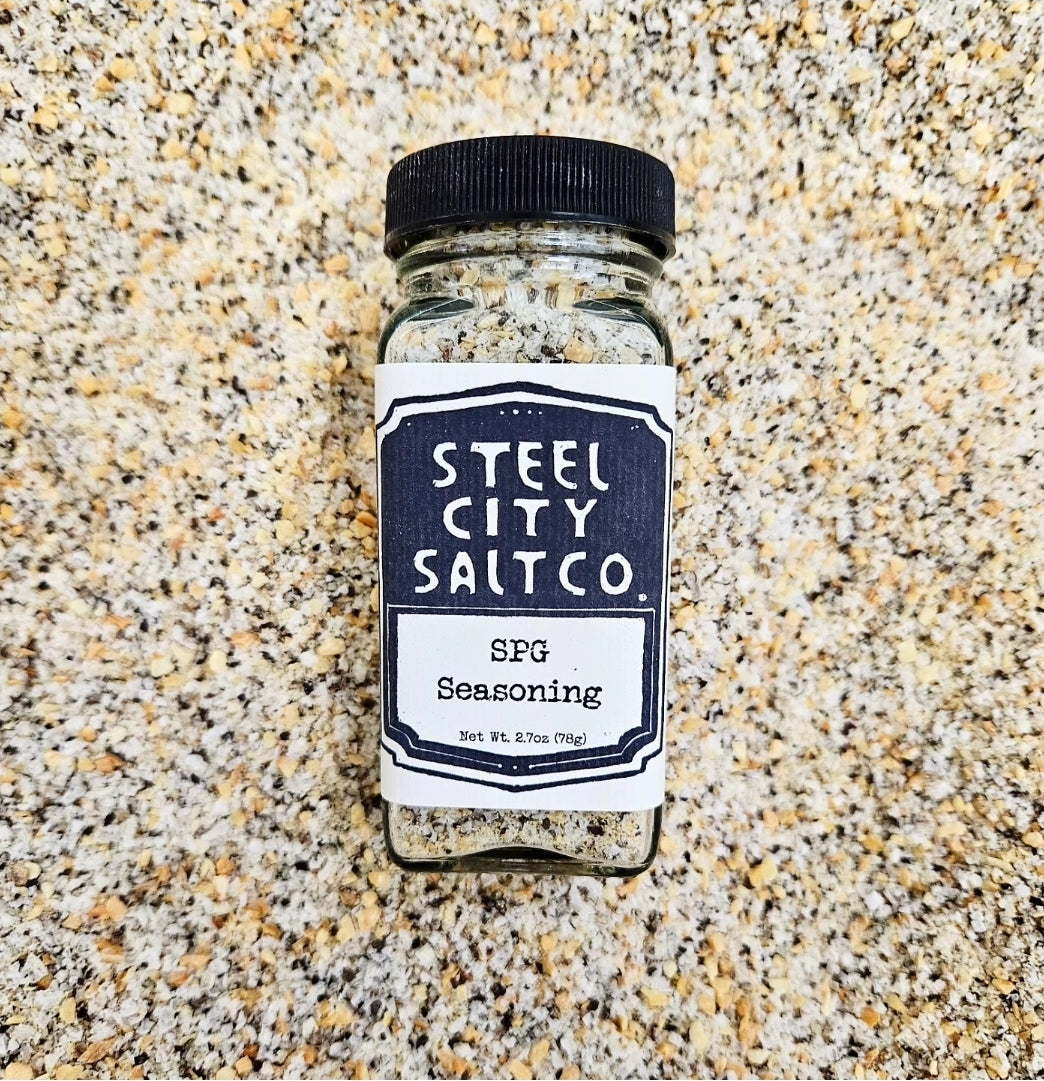 A clear spice jar labeled &quot;SPG Seasoning&quot; stands upright on a textured surface, blending with the all-purpose salt, pepper, and garlic mix inside.