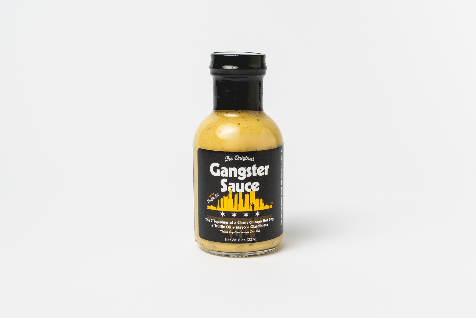 A bottle of Gangster Sauce Chicago hot dog sauce stands upright on a white background, featuring a black label with a yellow city skyline and white text.