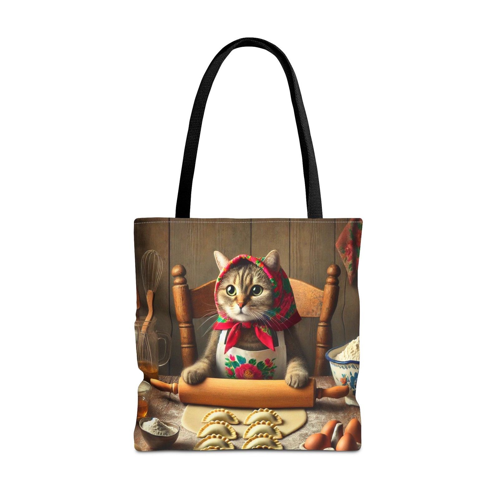 The Polish Cat Making Pierogi Tote Bag in black features a cute cat in a floral scarf rolling dough at a table, surrounded by baking ingredients and shaped cookies.