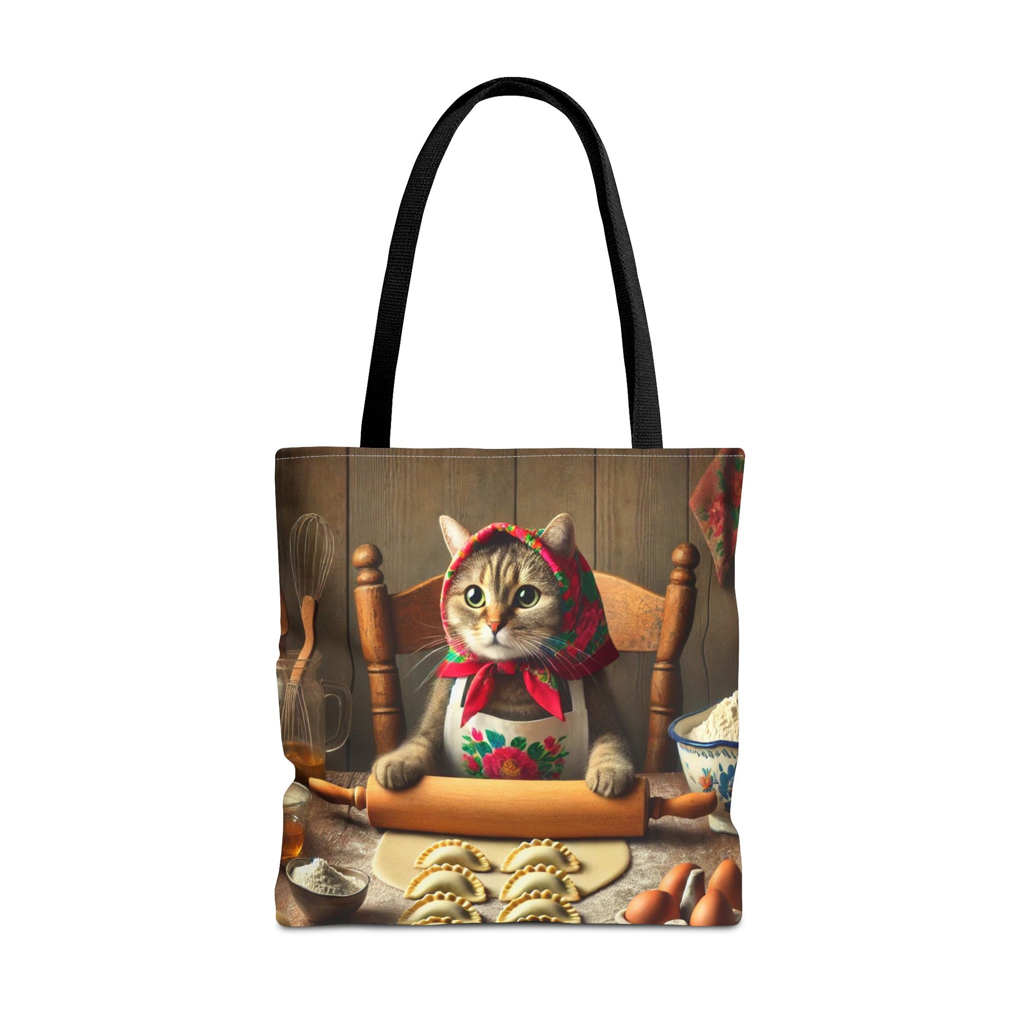 The Polish Cat Making Pierogi Tote Bag in black features a cute cat in a floral scarf rolling dough at a table, surrounded by baking ingredients and shaped cookies.
