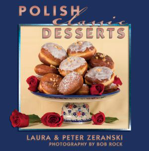 A plate of glazed Polish desserts and pastries is displayed on a decorative stand with red roses, featuring the book title &quot;Polish Classic Desserts&quot; above and authors Laura &amp; Peter Zeranski below the image.