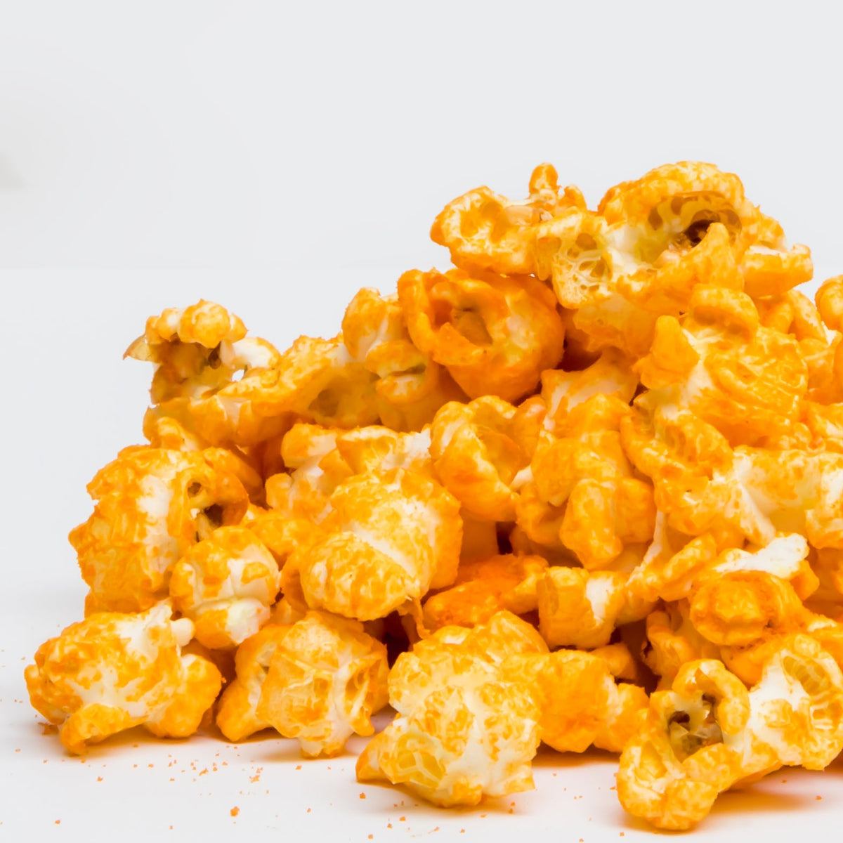 A pile of Jalapeño Cheddar Popcorn is scattered on a white surface.