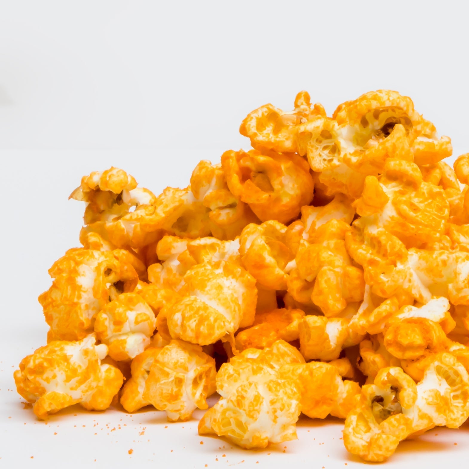 A pile of Jalapeño Cheddar Popcorn is scattered on a white surface.