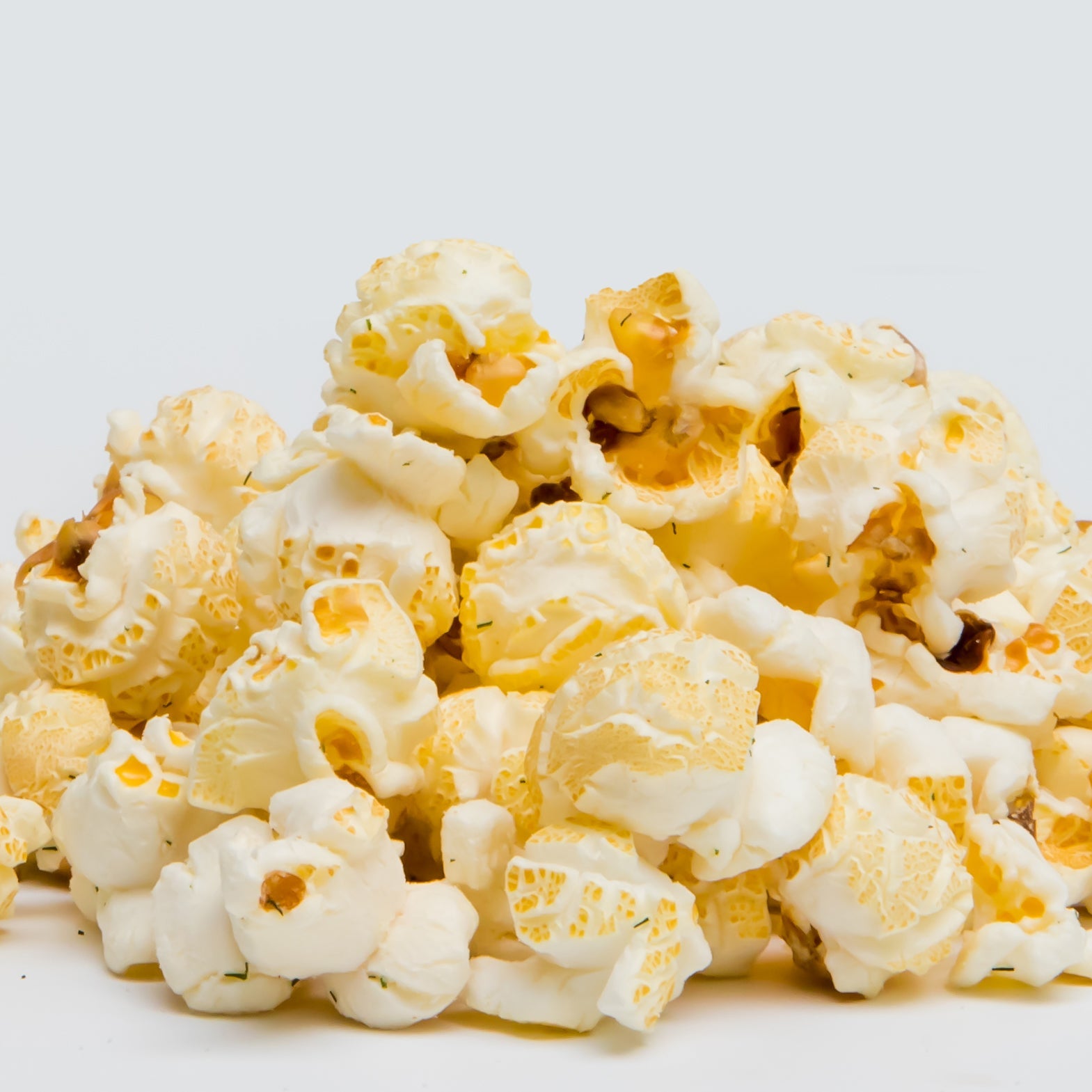 A pile of Dill Pickle Popcorn, made with non-GMO kernels and bursting with tangy dill pickle flavor, sits on a plain white background.