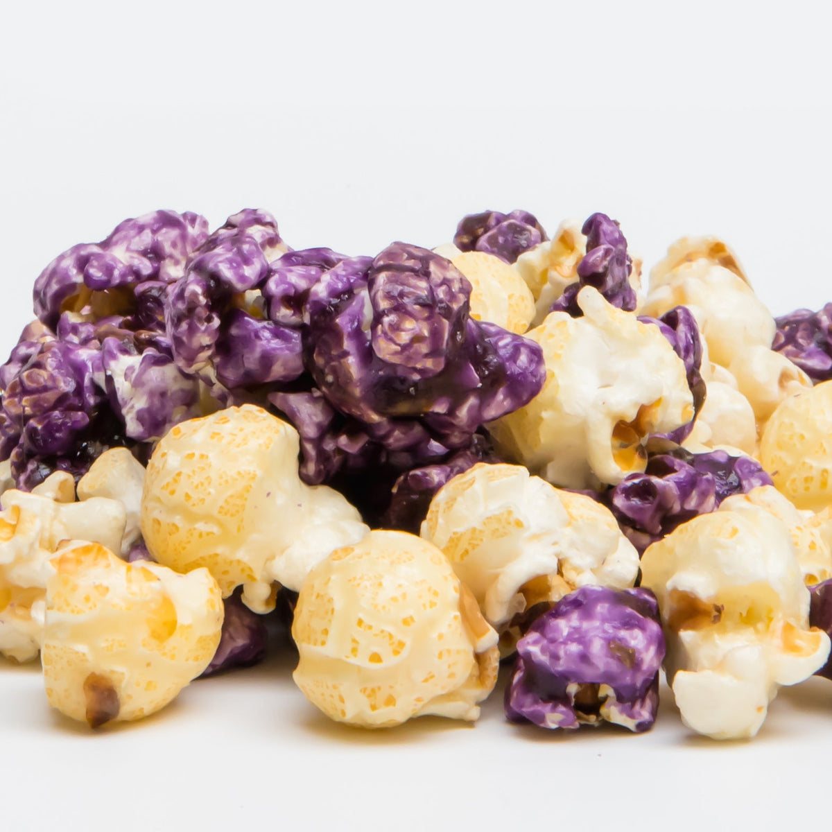 A mound of Blueberry Cheesecake Popcorn—white and purple-coated, made with non-GMO popcorn—rests on a white background, ideal for fans of this sweet treat.