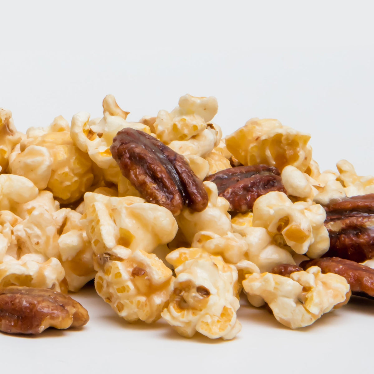 Butter Pecan Popcorn featuring caramel-coated popcorn and glazed pecan halves is displayed in a small pile against a plain white background.