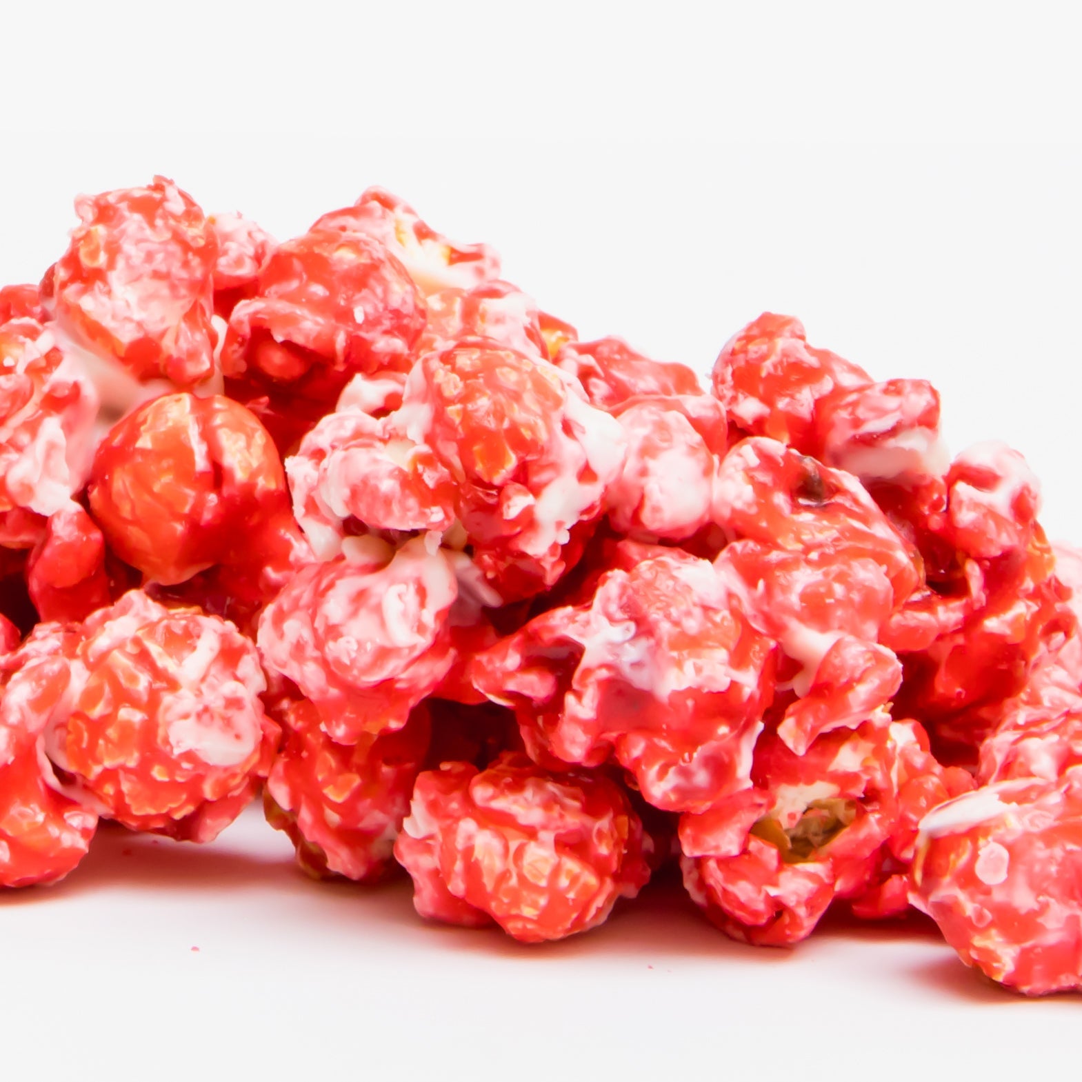 Raspberry White Chocolate Popcorn is shown in a pile of red and white candy-coated pieces against a plain white background.