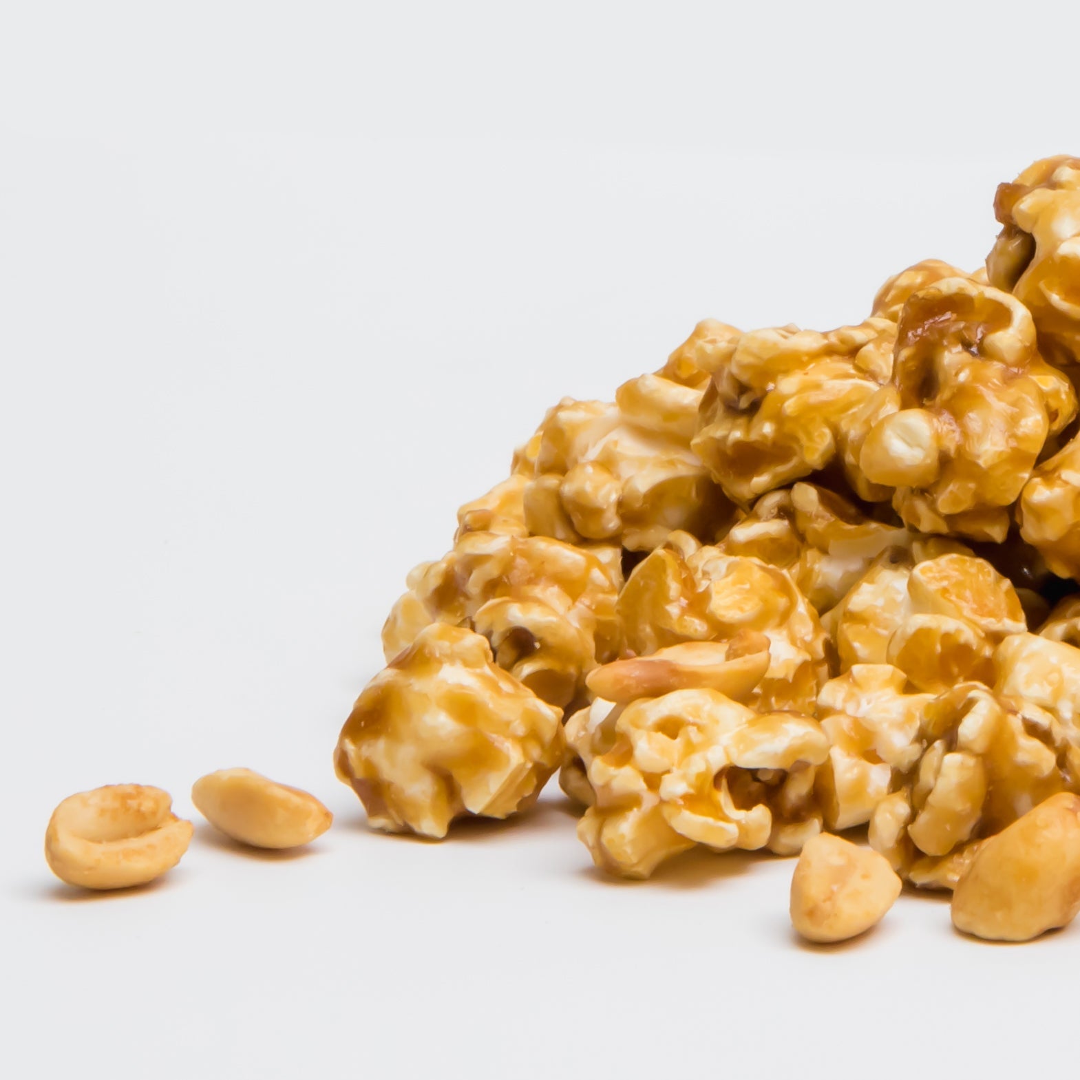 Caramel Peanut Popcorn is shown on a plain white background, with golden caramel-coated popcorn mixed with crunchy sea salted peanuts.