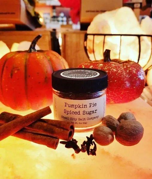 A jar of Pumpkin Pie Spiced Sugar sits among pumpkins, cinnamon sticks, nutmeg, and star anise—crafted with organic cane sugar for a cozy autumn feel. Ideal for adding to your favorite pumpkin spice blend recipes.
