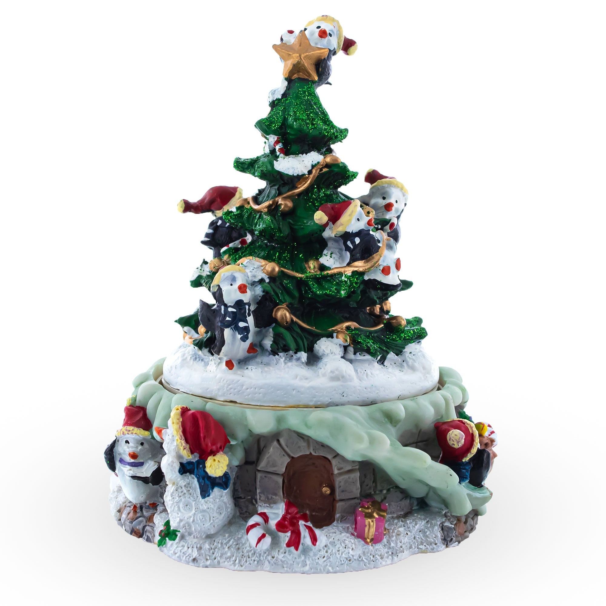 A festive musical figurine featuring penguins decorating a spinning Christmas tree atop a snow-covered cottage, adorned with gifts and holiday accents, set against a white background.